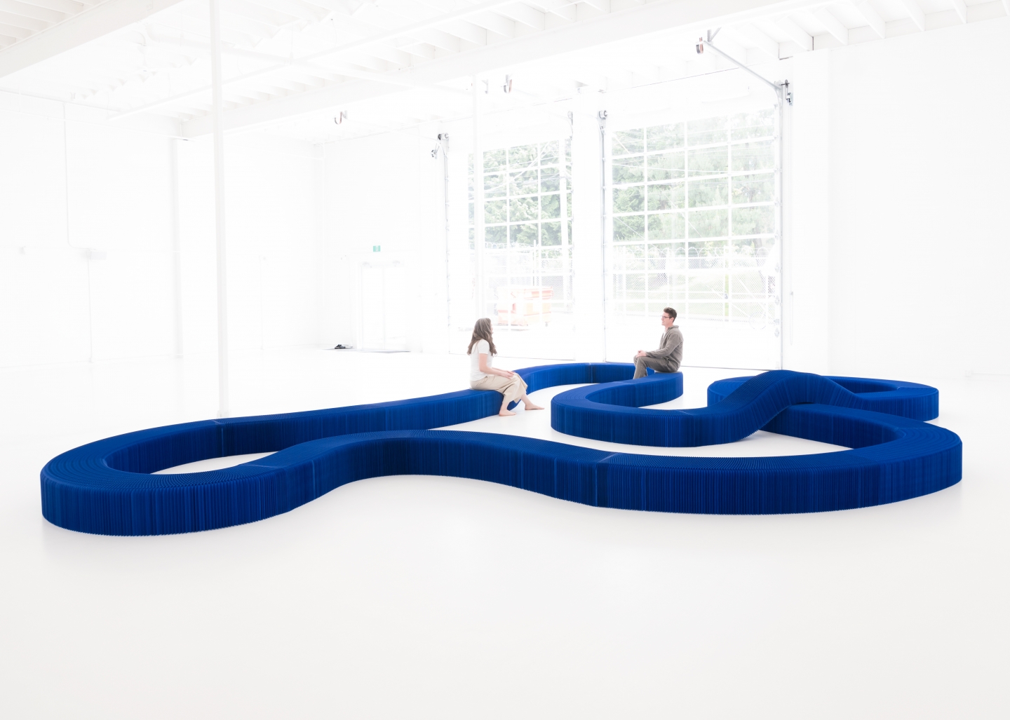 Two people sit on a serpentine bench made from connected softseating fanning stools.