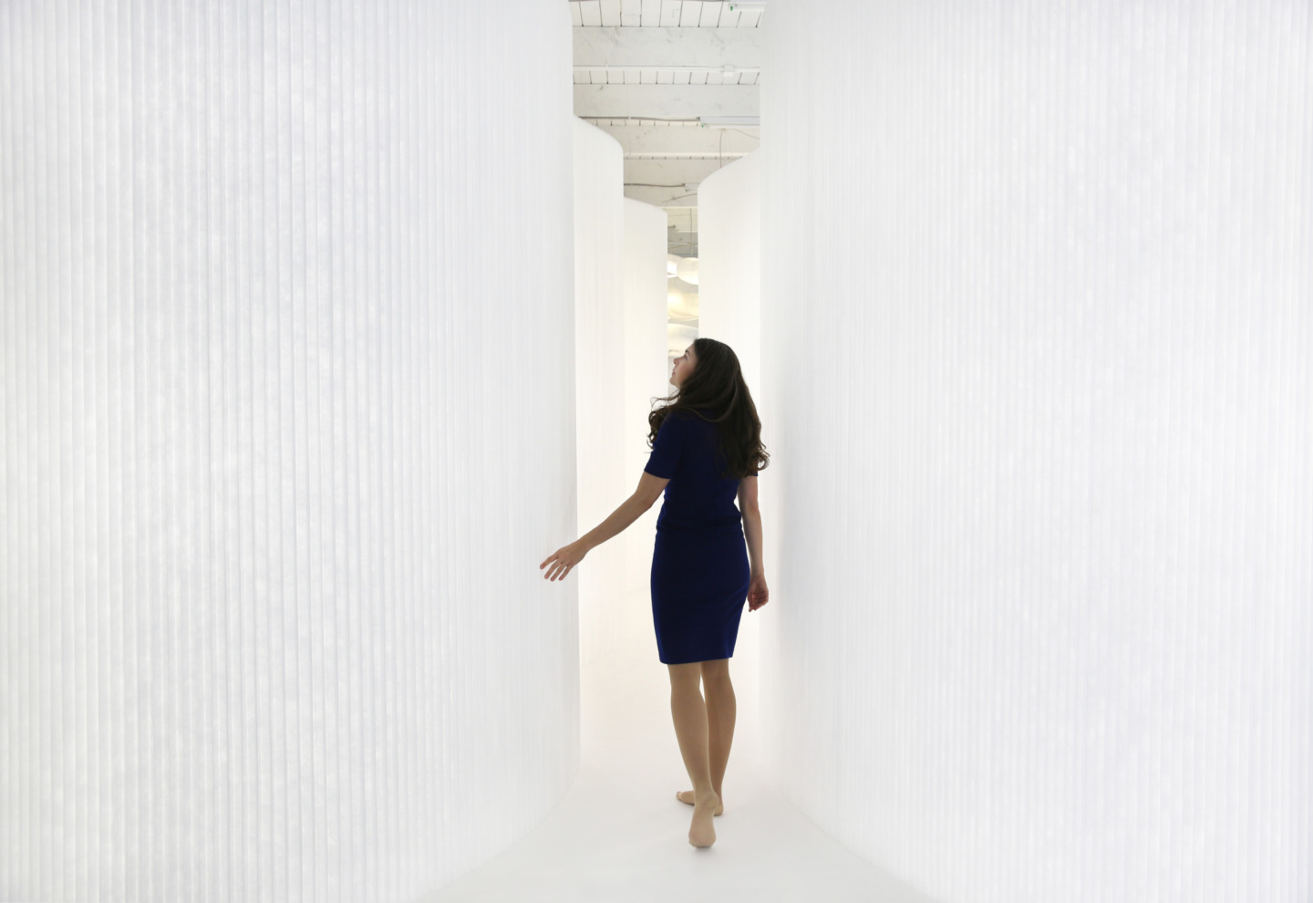 woman runs a hand along the fins of a white textile softwall - moveable wall partitions by molo