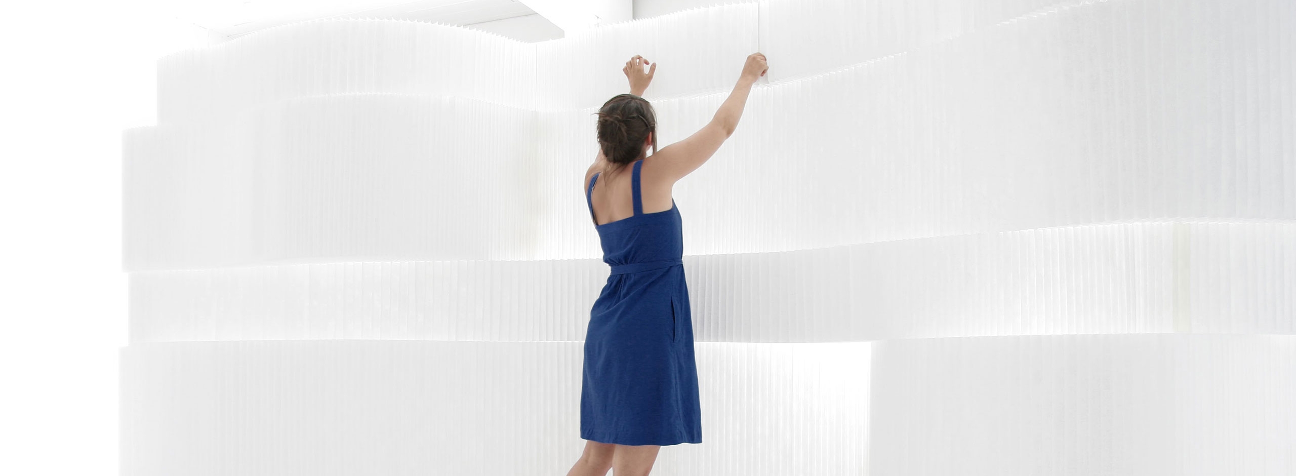 woman wearing a blue dress adjusts stacked white textile softblocks