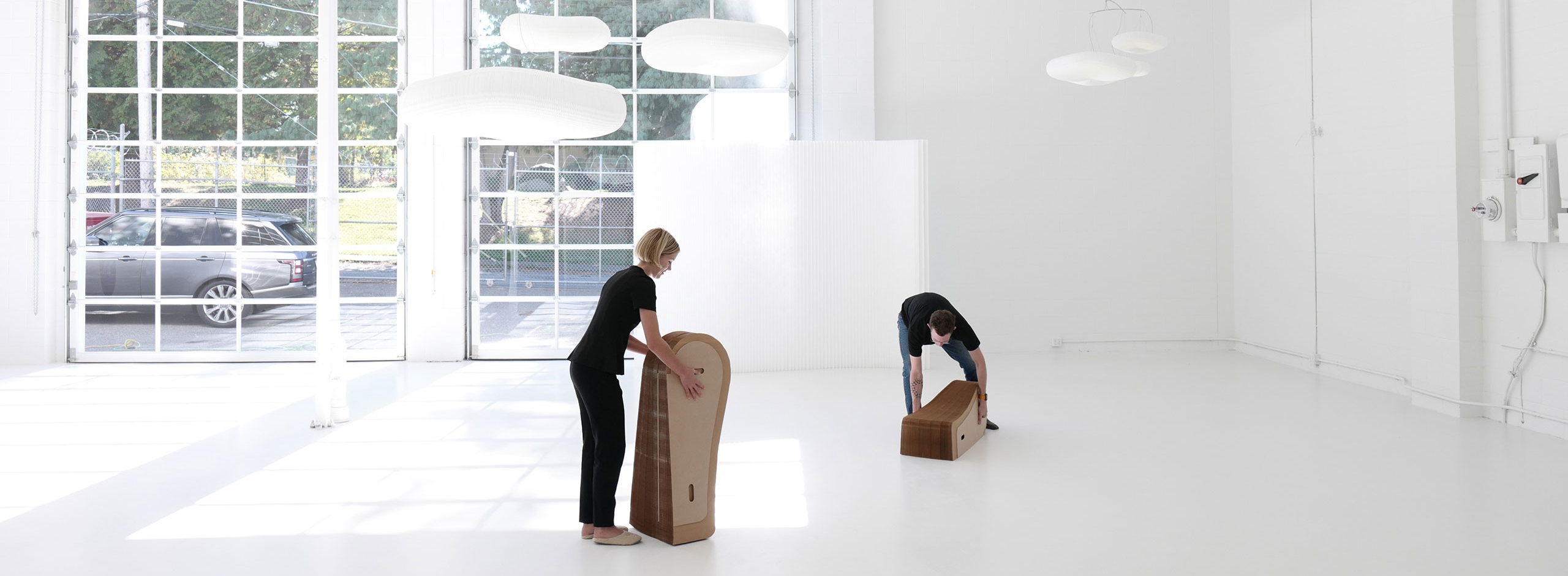 Folding paper furniture, two people compress a softseating lounger for storage.