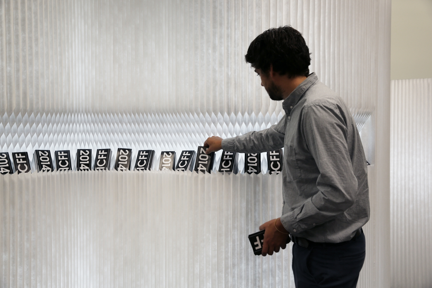 portable wall partition in white by molo - a man retrieves a postcard from a display cut into a softwall