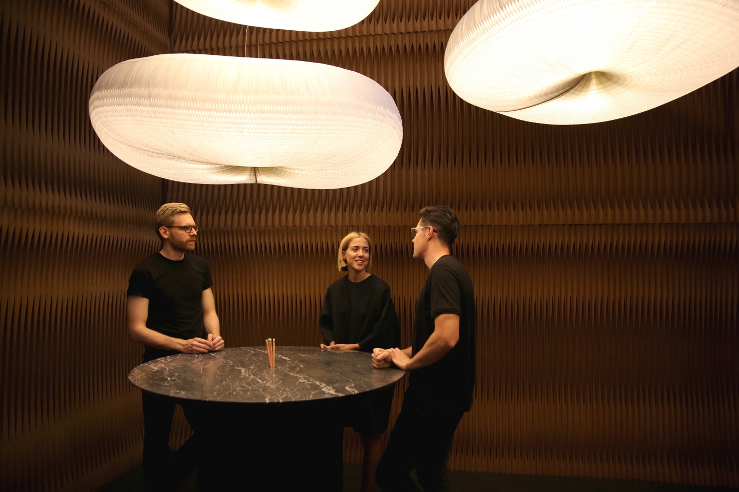paper lighting and accordion paper furniture by molo - a group chats around a cantilever table with a black marble top, beneath a canopy of clouds
