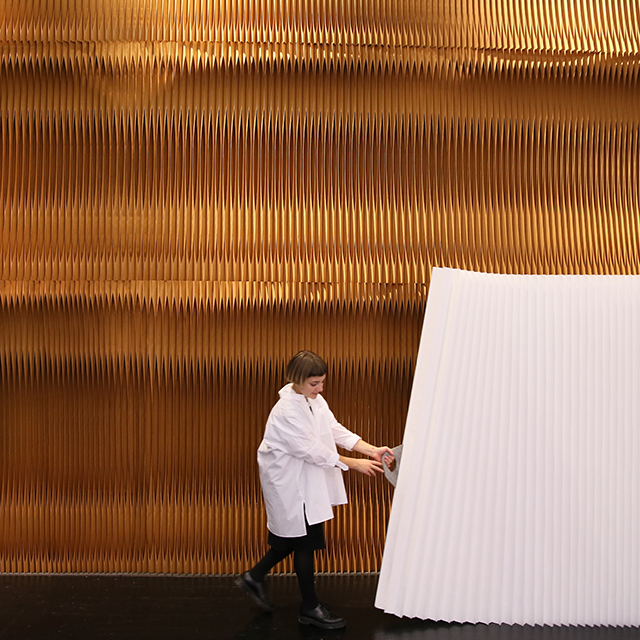 white accordion wall partition by molo - a woman pulls open a textile softwall at Orgatec 2016