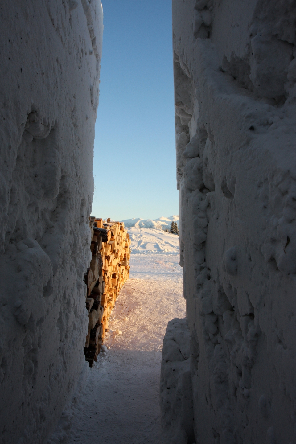 stacked firewood rests beside an opening between towering walls of snow. northern sky circle was an installation in Alaska designed by Stephanie Forsythe + Todd MacAllen, in collaboration with sound artist Ethan Rose.