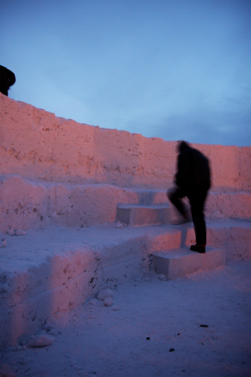 stacked firewood rests beside an opening between towering walls of snow. northern sky circle was an architectural, snow and ice maze installation in Alaska designed by Stephanie Forsythe + Todd MacAllen, in collaboration with sound artist Ethan Rose.